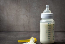 A baby bottle filled with milk next to a scoop of powdered formula