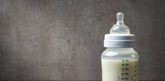 A baby bottle filled with milk next to a scoop of powdered formula
