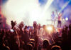 Concert crowd with hands raised, bright stage lights.