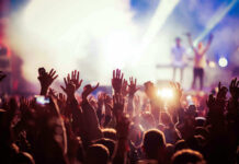Concert crowd with hands raised, bright stage lights.
