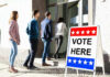 People entering building with Vote Here sign nearby.