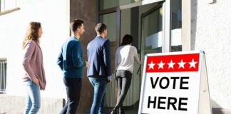 People entering building with Vote Here sign nearby.