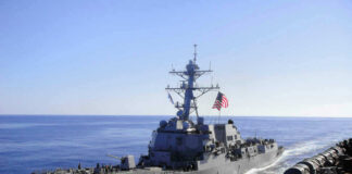 Warship with American flag sailing in the ocean.