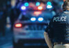Horror Erupts: Child Hit In Mass Shooting Police officer stands near patrol car with lights flashing.