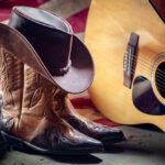 VIDEO: Country Music StarTopples Pop Royalty Cowboy boots and hat with guitar and flag.