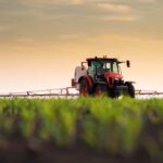 A tractor spraying crops in a field during sunset