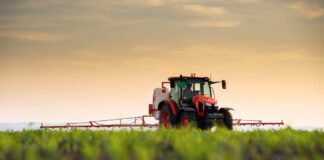 A tractor spraying crops in a field during sunset