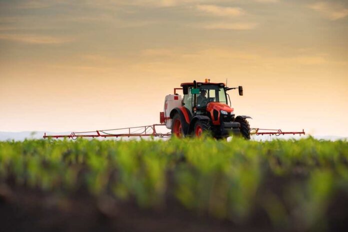 Tractor,Spraying,Pesticides,On,Corn,Field,With,Sprayer,At,Spring A tractor spraying crops in a field during sunset