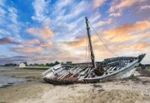 An abandoned boat on a sandy shore during sunset