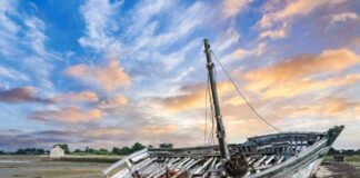 An abandoned boat on a sandy shore during sunset