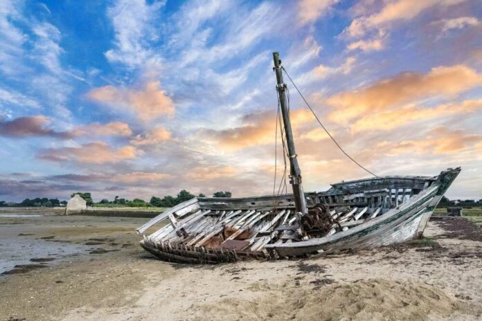 An abandoned boat on a sandy shore during sunset