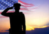 Silhouette of soldier saluting in front of flag