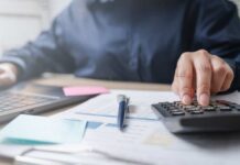 Person using a calculator while working on a laptop and reviewing documents