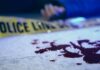 Blood on pavement with police tape and a hand in the background