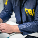 FBI Agents Exposed? Spouses Listed – Outrage Brewing Person in FBI jacket working on laptop.