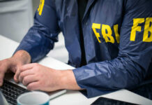 FBI Agents Exposed? Spouses Listed – Outrage Brewing Person in FBI jacket working on laptop.
