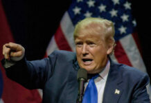 Trump’s Grand Conspiracy Boss Bails – No Charges Man pointing while speaking at podium with American flags.