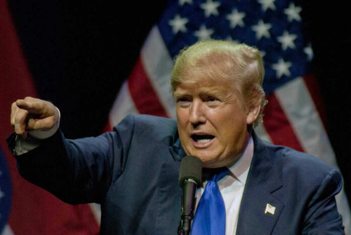 shutterstock_717752995 Man pointing while speaking at podium with American flags.