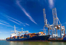 Two Ships Down – Crew Vanish Cargo ship docked at port with cranes unloading.
