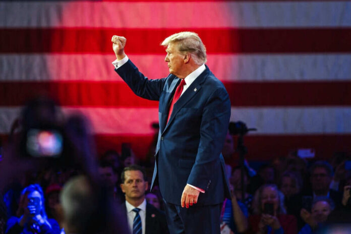 Donald Trump raises a fist on stage before a large U.S. flag