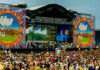 A large crowd at an outdoor music festival with a vibrant stage