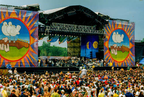 A large crowd at an outdoor music festival with a vibrant stage