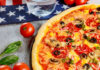 Pizza with pepperoni, olives, mushrooms, and vegetables on a table