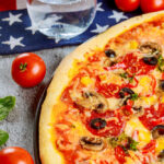 Pizza with pepperoni, olives, mushrooms, and vegetables on a table