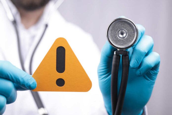 The,Doctor,With,Medical,Gloves,Holding,The,Papercut,Of,An Doctor with stethoscope holding a warning sign