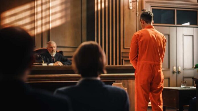 Court,Of,Law,And,Justice,Trial,Proceedings:,Law,Offender,In Defendant in orange jumpsuit stands before a judge in a courtroom