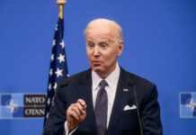 Joe Biden speaking at a podium with a blue NATO backdrop