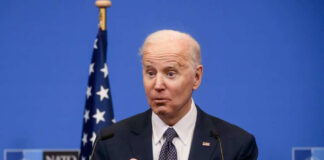 Joe Biden speaking at a podium with a blue NATO backdrop