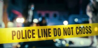 Police line caution tape at a crime scene with blurred figures in the background
