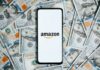 Smartphone with Amazon logo on screen over US hundred-dollar bills