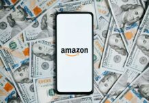 Smartphone with Amazon logo on screen over US hundred-dollar bills