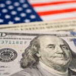 Close-up of a hundred dollar bill in front of an American flag