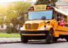 Yellow school bus parked by a campus sidewalk