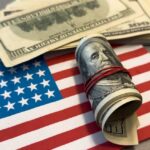 A roll of hundred dollar bills placed on an American flag